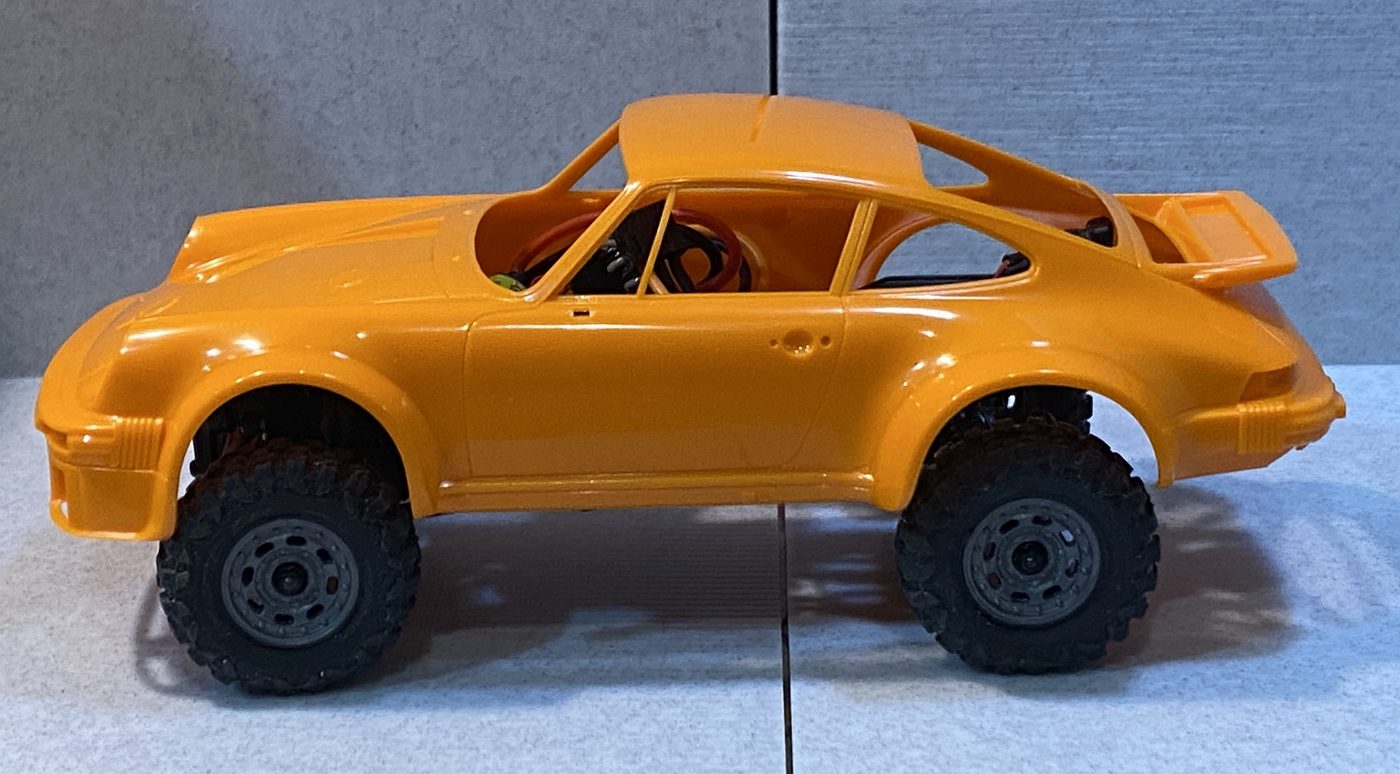 An orange Porsche 911 body set on the chassis, wheels roughly aligned with the arches.
