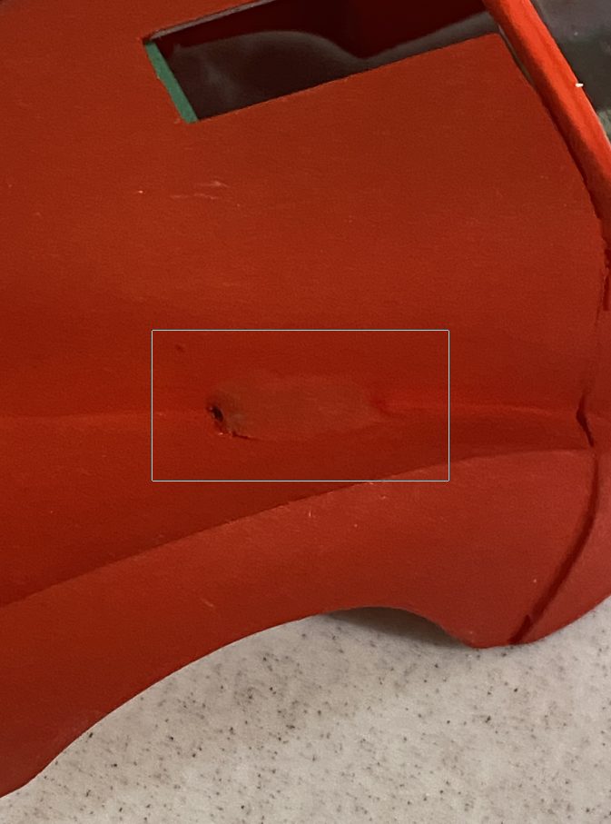 Close view of a painted orange hood with a small area where the plank shows through, boxed for emphasis.
