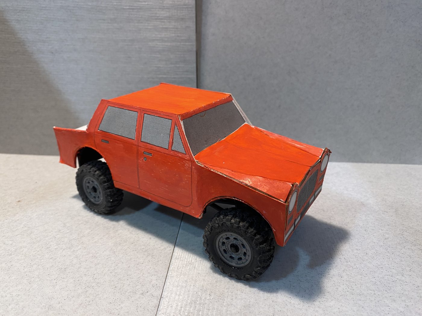 An orange paper body, folded and painted, mounted on the crawler chassis.